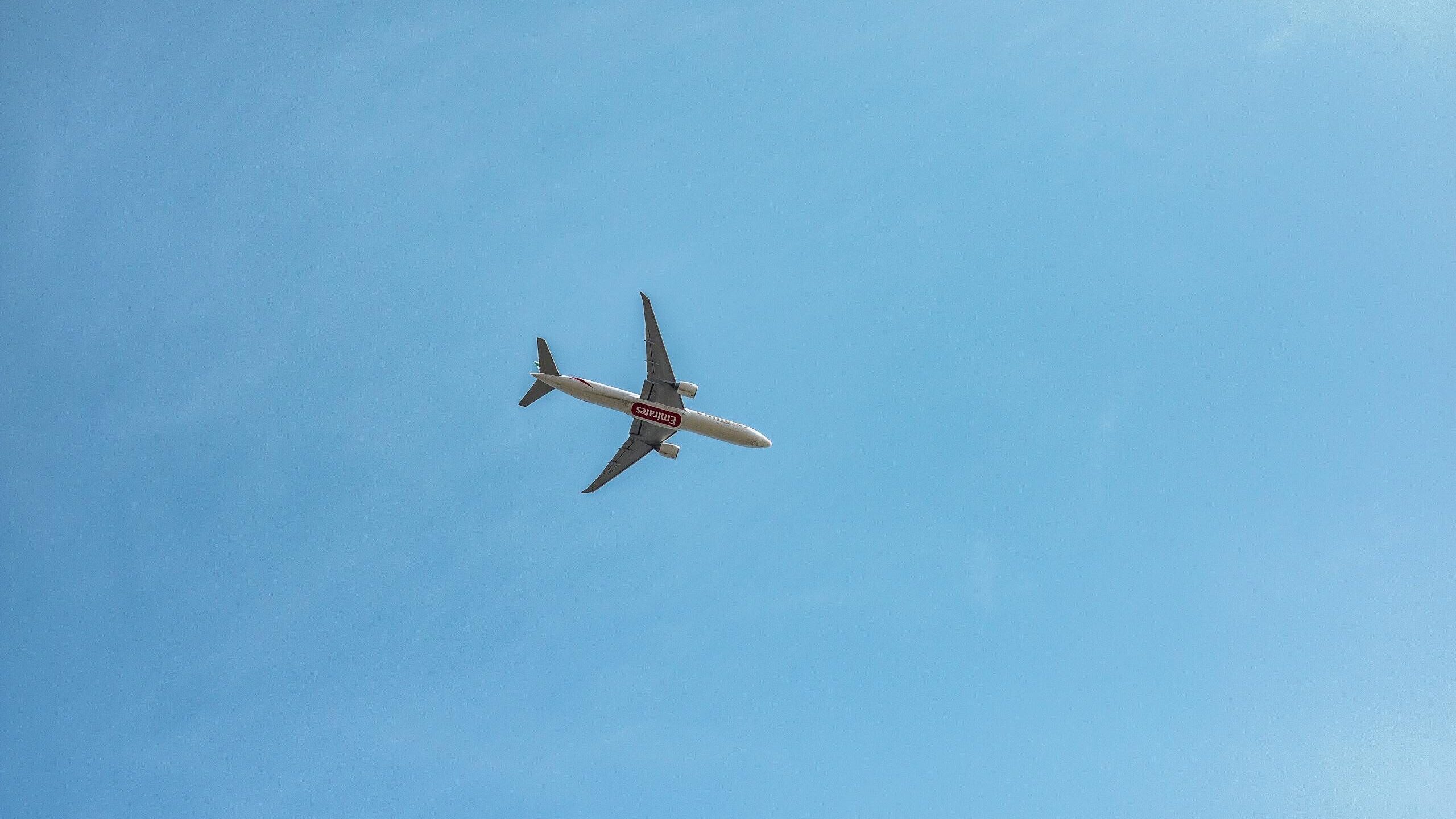 A commercial airplane flying high against a clear blue sky, viewed from below.